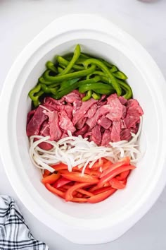 a bowl filled with meat and vegetables on top of a white counter next to a napkin