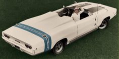 a woman sitting in the driver's seat of a white and blue muscle car