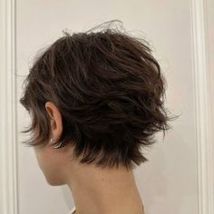 the back of a woman's head with short brown hair in front of a white wall