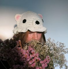 a woman wearing a crocheted bear hat with flowers in front of her face