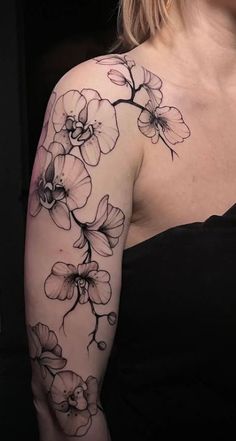 a woman wearing a black dress with flowers on her arm and shoulder, in front of a dark background