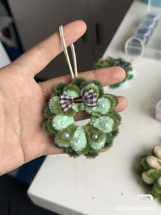 a hand holding a green wreath ornament with a bow on it's head