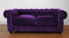 a purple couch sitting on top of a hard wood floor next to a white wall