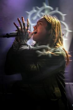 a man with long hair holding his hands up in the air while singing into a microphone