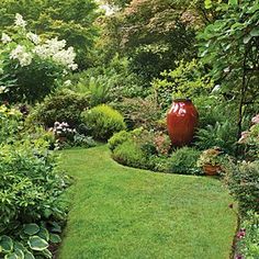 a lush green garden with lots of flowers and plants in the center, along with a path leading to a large red vase