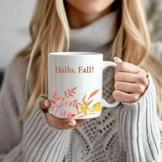 a woman holding a coffee mug with the words hello fall on it