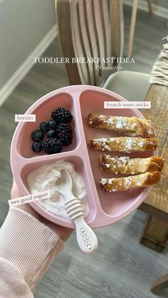 a person holding a pink plate with food on it that includes french toast and berries