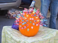 an orange vase filled with lots of candy on top of a table next to a person