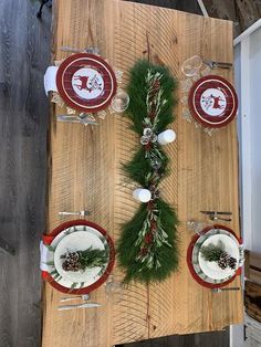 the table is set for christmas dinner with pine cones and greenery on it, along with other place settings