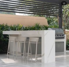 an outdoor kitchen with marble counter tops and barstools, surrounded by greenery