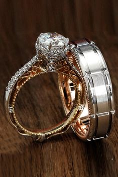 two wedding rings with diamond accents on top of each other, sitting on a wooden surface