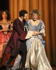 two people dressed in period costumes standing on stage with one holding the other's hand