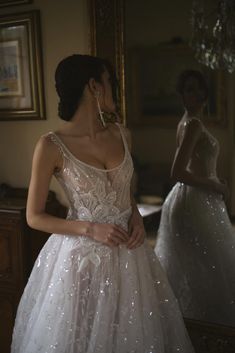 a woman in a wedding dress looking at herself in the mirror with her hand on her hip