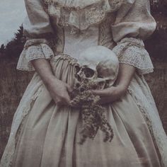 an old photo of a woman holding a skull in her hands and wearing a dress