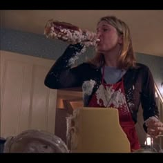 a woman standing in front of a counter drinking from a plastic bottle with sprinkles on it