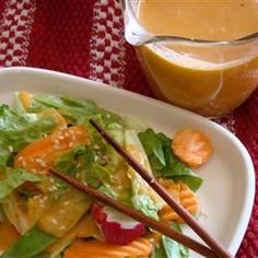 a white plate topped with salad and chopsticks next to a jar of orange juice