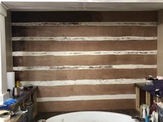 a bath tub sitting next to a wall covered in wood planks with paint all over it