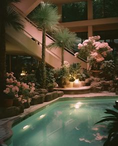 an indoor swimming pool surrounded by palm trees and flowers in the night time with lights on