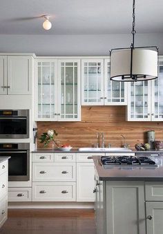 a large kitchen with white cabinets and wood paneling on the walls, along with an island