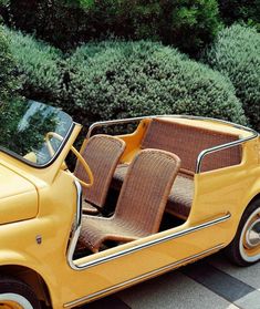 an old yellow car is parked in front of some bushes and shrubbery with the door open