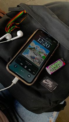 a cell phone sitting on top of a backpack with ear buds and headphones attached to it