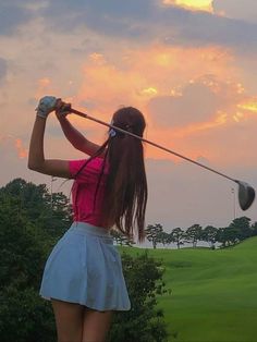 a woman is playing golf at sunset on the green grass with trees in the background