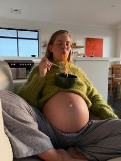 a pregnant woman sitting on a couch eating noodles