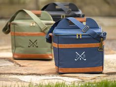 three different colored cooler bags sitting on top of a stone slab next to grass and trees