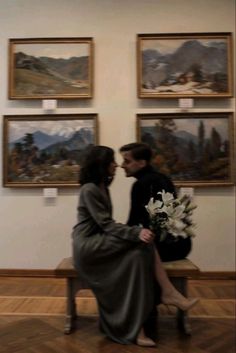 a man and woman sitting on a bench in front of some paintings with white flowers