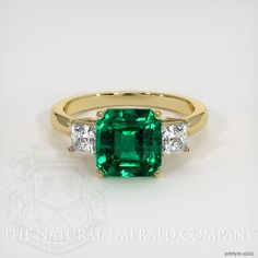 an emerald and diamond ring with three diamonds on the side, set in yellow gold