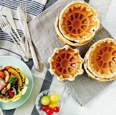 three waffles on plates with forks and spoons next to them, along with other food items