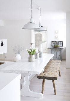 a white table and bench in a room with wood flooring, two lights hanging from the ceiling