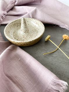 a white bowl sitting on top of a table next to a pink scarf and flower