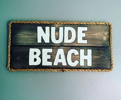 a wooden sign that says nude beach hanging on the wall