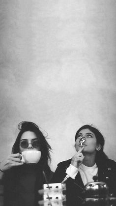 two women sitting at a table with cups in their hands and one holding a spoon to her mouth