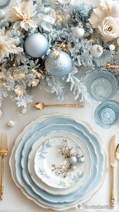 a table set with blue and white plates, silverware and christmas tree branches in the background