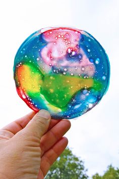 a hand holding a soap bubble in front of a sky filled with clouds and stars