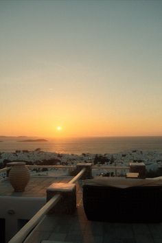 the sun is setting over an ocean with chairs and tables on it's patio