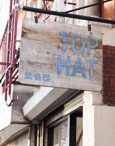 a wooden sign hanging from the side of a building that says top hat on it