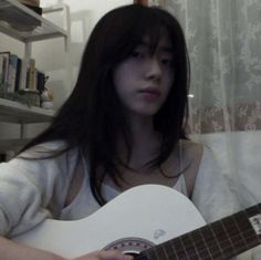 a girl with long black hair is holding a guitar