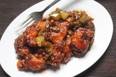 a white plate topped with meat covered in sauce next to a knife and fork on top of a table