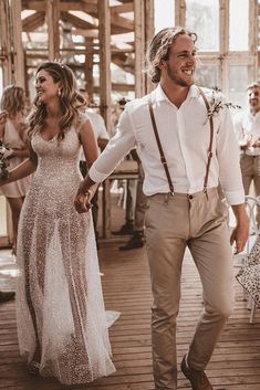 a man and woman holding hands walking down a wooden floor with other people in the background