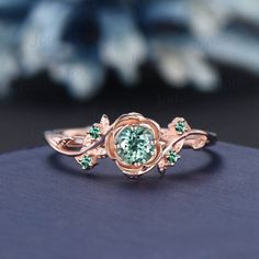 a close up of a ring with a green stone in the center and leaves around it