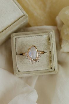 an engagement ring sits in a box on a white cloth with flowers and petals around it