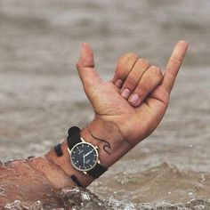 a man with a wrist tattoo holding his hand up in the water while wearing a watch