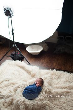 a newborn baby is laying on a fluffy rug in front of a camera set up