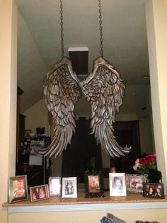 two angel wings hanging from the ceiling above a mantle with pictures and frames on it