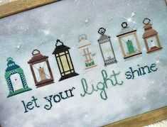 a cross stitch picture with the words let your light shine on it and four lit lanterns