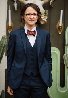 a woman in a suit and bow tie standing next to cactuses with horns on the wall behind her