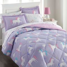 a purple bed with unicorns on it in a bedroom next to a pink lamp